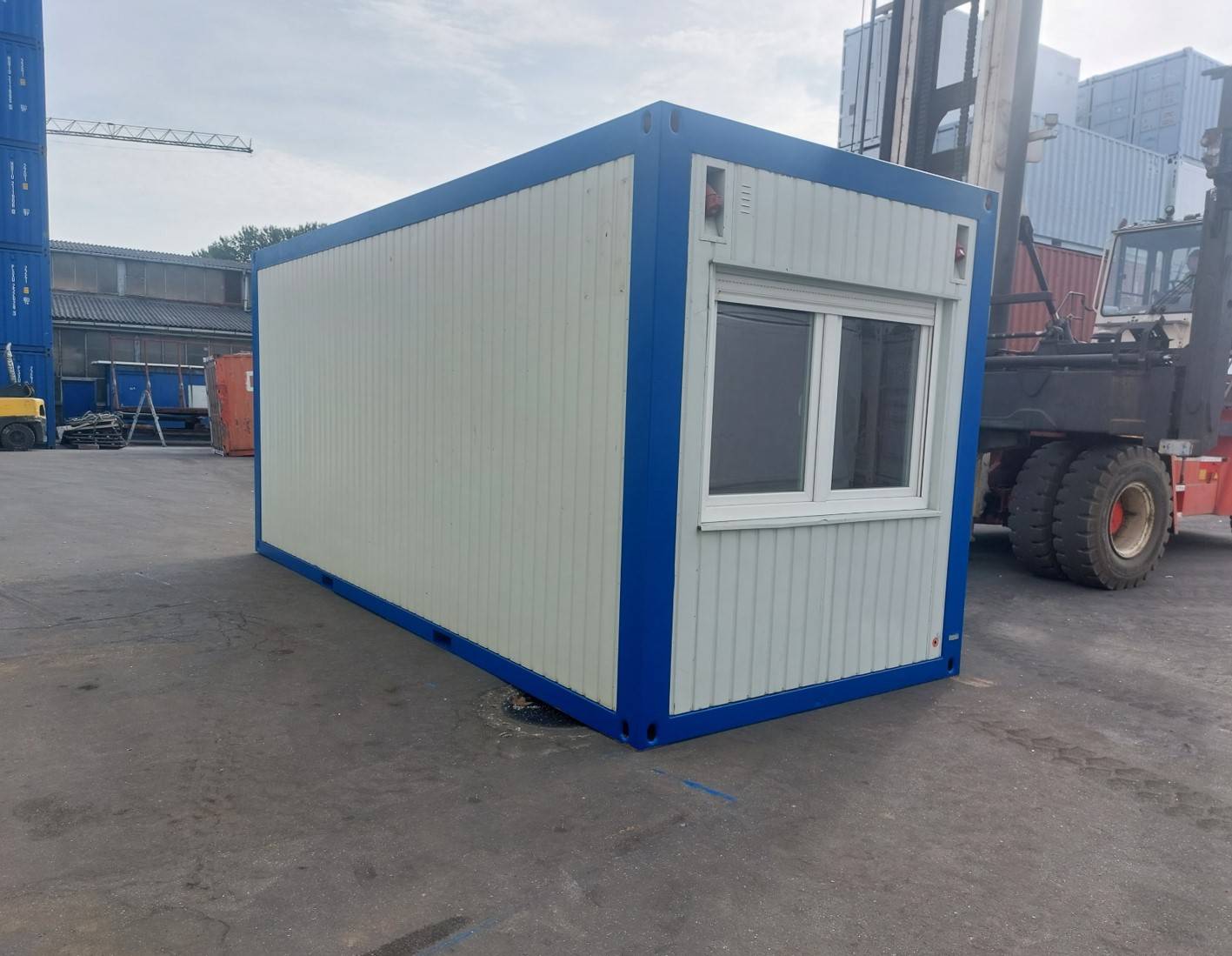 Ein weißer 20-Fuß-Bürocontainer mit blauem Rahmen und einem Fenster auf einer der kürzeren Seiten.
